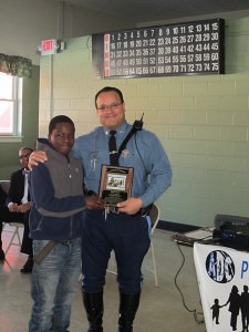 Thirteen-year-old Abdi Adan gives an appreciation award to Massachusetts State Trooper Orlando Medina at the event at Riverview Apartments. 