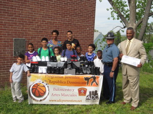 State Trooper Orlando Medina delivered a $300 check from the Massachusetts State Police Association to help fund the sneaker drive for Dominican Republic children. Participants celebrate at Duggan Park Apartments.