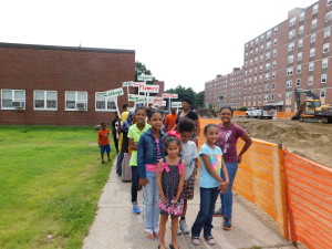 Children in the youth program at Riverview Apartments walk towards the community garden with the signs they made for elderly gardeners.